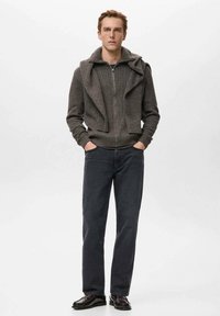 Sudadera gris de punto acanalado con cremallera y cuello doblado, combinada con vaqueros oscuros y zapatos negros. Textura rugosa y diseño moderno.