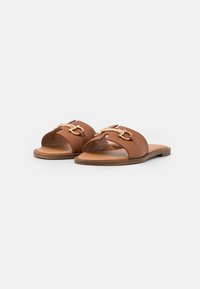 Brune læder slide sandaler med åbne tæer, der har guldfarvede hardware-accenter og en flad sål. Minimalistisk design med en glat overflade.