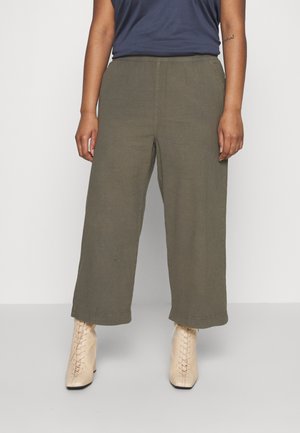 Pantaloni larghi verde oliva con una texture liscia, dotati di una cintura semplice e orlo dritto, abbinati a stivali beige con tacco.