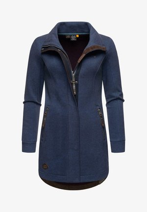 Tume sinine jakk kõrge kaelusega, täispikk tõmblukk ja kaks külgetõmblukku. Omab tihedat lõiget ja tekstuurset kangast pruunide detailidega.