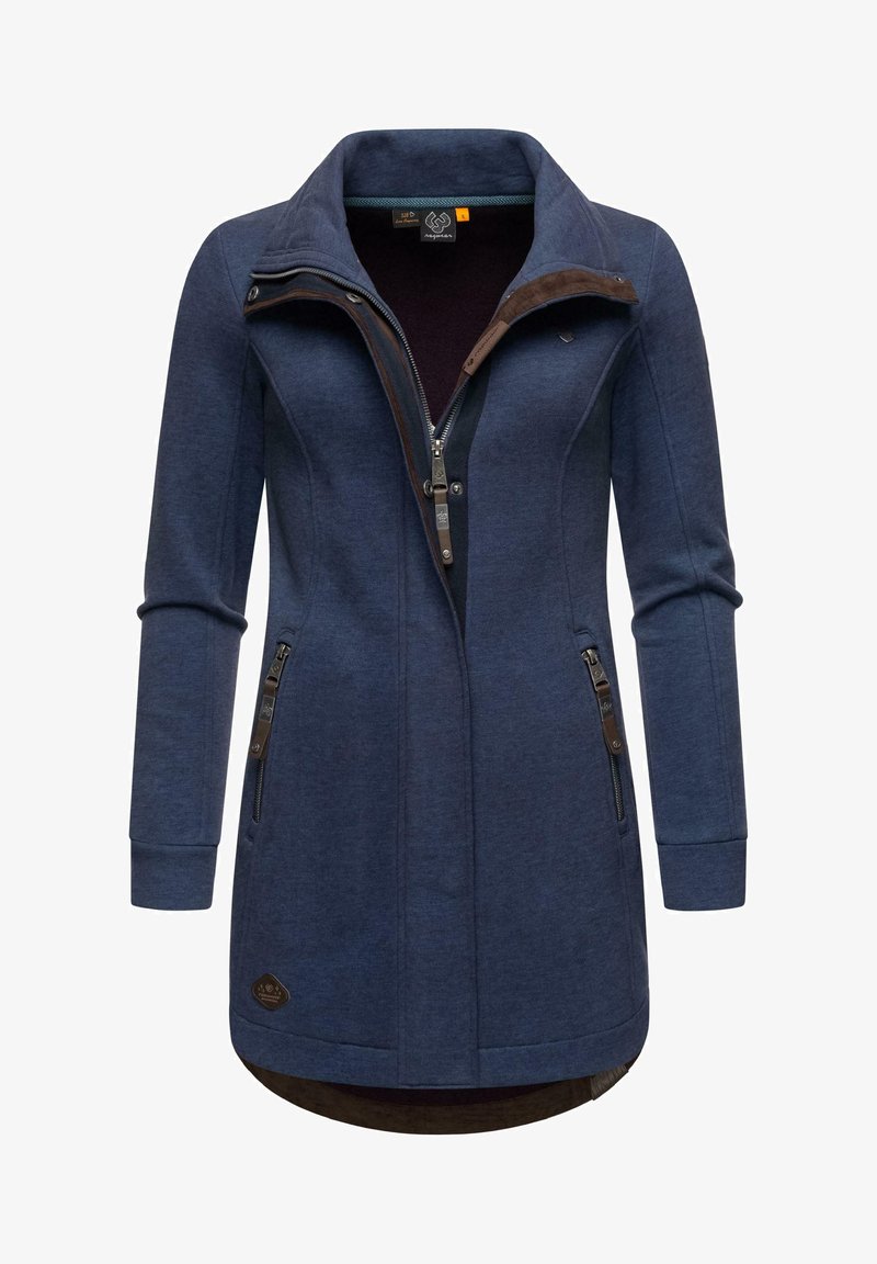 Tumši zilas krāsas jaka ar augstu apkakli, pilnu rāvējslēdzēju un diviem sānu rāvējslēdzējiem. Iezīmējas ar pieguļošu piegriezumu un struktūrvielu ar brūnām akcentiem.