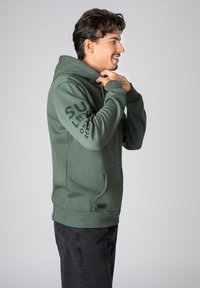 Groene hoodie met een kangaroo-pocket, ribgebreide manchetten en een geprinte logo op de mouw. Zacht materiaal met een gladde textuur.