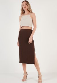 Un top scurt ribbed de culoare bej deschis, purtat cu o fustă midi ajustată de culoare brună, cu fente laterale. Modelul poartă sandale cu toc în culori neutre.