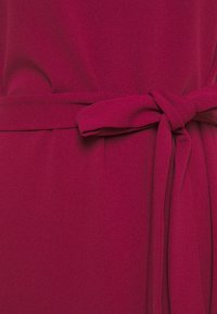 Fuksjowa sukienka o miękkiej fakturze, z wiązanym paskiem w talii i gładkim, lejącym się materiałem, tworzącym elegancką sylwetkę.