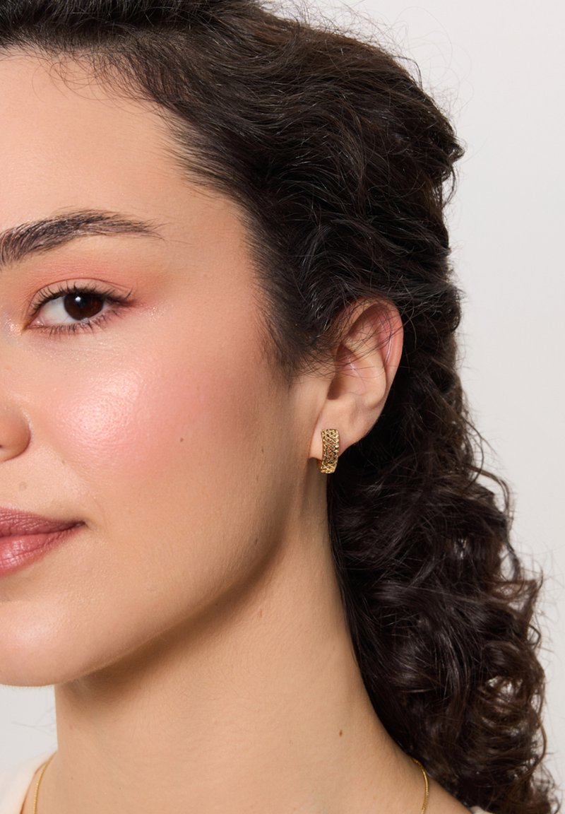 Złota kolczyk w kształcie obręczy z teksturowanym wzorem, z plecionym motywem. Kompaktowy kształt, odpowiedni do codziennego noszenia, podkreślający ucho.