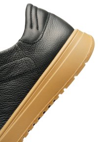 Black leather sneaker with a textured upper, featuring a tan rubber sole and subtle stitching details along the heel.