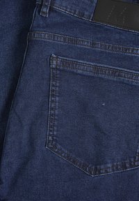 Mörkblå denimjeans med en bakficka med sydd kant, en synlig läderetikett vid midjebandet och en slät textur.