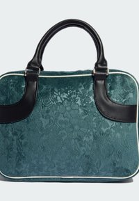 Sac à main en velours émeraude foncé avec des poignées en cuir noir et des bordures décoratives blanches. Forme structurée avec une surface texturée.