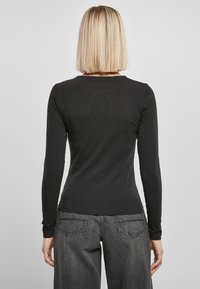 Sort langærmet skjorte lavet af blødt stof, med en rund halsudskæring og en tætsiddende pasform, parret med grå, løs pasform jeans.
