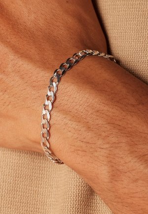 Silver metal chain bracelet with interlocking links, featuring a smooth finish and a polished surface. Worn on a wrist against textured fabric.