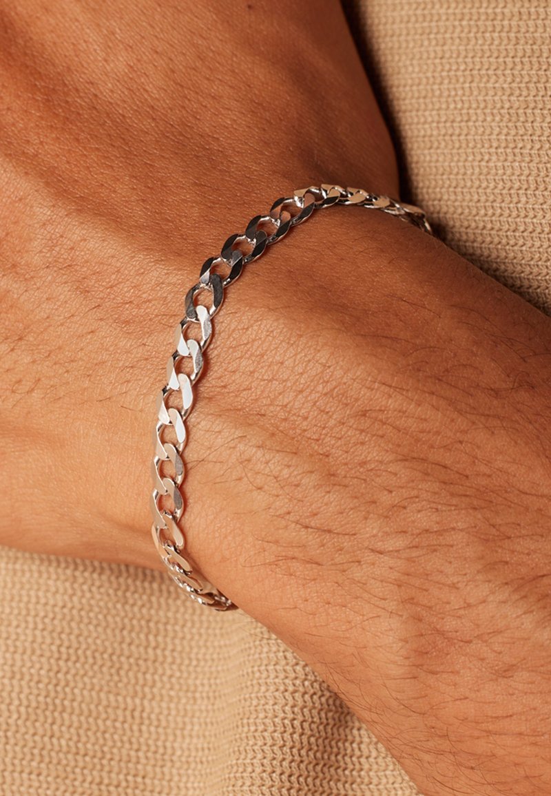Silberne Metallkette Armband mit ineinandergreifenden Gliedern, ausgestattet mit einer glatten Oberfläche und einer polierten Fläche. Am Handgelenk gegen strukturierten Stoff getragen.