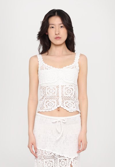 Ensemble top et jupe en crochet blanc, avec des bords festonnés, des motifs carrés et une texture en maille ouverte. Conçu avec un cordon de serrage ajustable.
