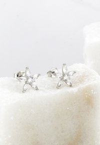 Silver blommformade örhängen med flera klara, fasetterade stenar. Designen inkluderar sex kronbladsliknande detaljer och en central ädelsten.