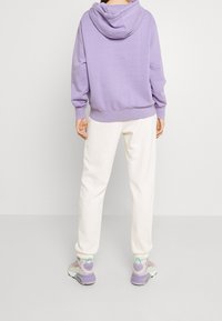 Lila hoodie med dragsnöre, parat med krämfärgade sweatpants och pastellfärgade sneakers med gröna och lila accenter.