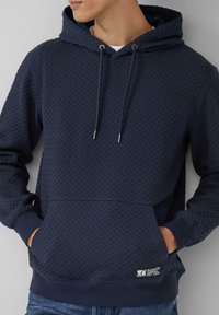 Granatowa bluza z kapturem o strukturze wzoru, z kapturem na sznurku, przednią kieszenią i ściągaczami na mankietach. Posiada oznaczoną metkę na dolnym brzegu.