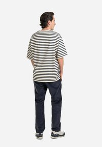Striped cotton t-shirt in cream and navy, loose fit with wide sleeves. Paired with dark pants and light sneakers, viewed from the back.