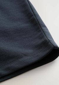 Gros plan sur un tissu bleu marine foncé, présentant une surface texturée avec un bord lisse et un ourlet contrasté à rayures sombres.