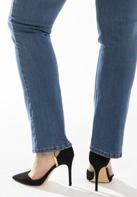 Chaussures à talons aiguilles en suedine noire avec un bout pointu et un design à lanière. Portées avec un jean en denim bleu, présentant un ourlet effiloché.