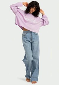 Sweatshirt scurt de lavandă deschis cu imprimeu grafic alb, asortat cu blugi evazati de culoare albastră deschis, cu talie înaltă. Material texturat și croi relaxat.