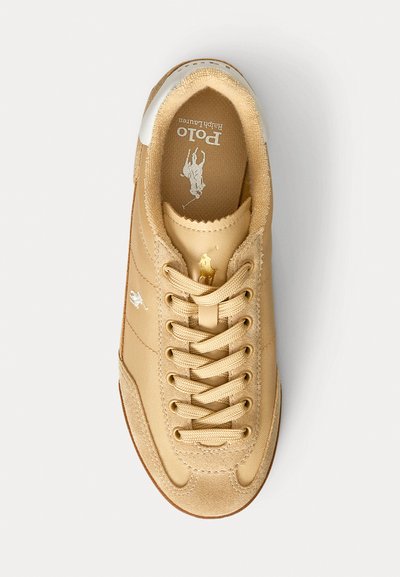 Sneaker low-top color beige con colletto imbottito, materiale in tela, punta rotonda, chiusura con lacci e branding discreto sulla linguetta e sul lato.