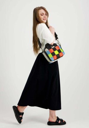 Nuori nainen kävelee valkoinen paita, musta hame, mustat sandaalit ja kantaa värikästä ruudullista olkalaukkua.