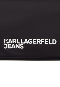 Crna tekstilna tkanina s bijelim natpisom "KARL LAGERFELD JEANS"; pravokutnog oblika, glatke teksture, minimalističkog dizajna s izraženom tipografijom.