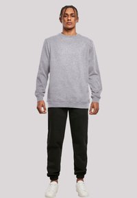 Grauer Sweatshirt mit langen Ärmeln, Rundhals und gerippten Bündchen. Kombiniert mit schwarzen Jogginghosen und weißen Sneakers, vor einem neutralen Hintergrund.