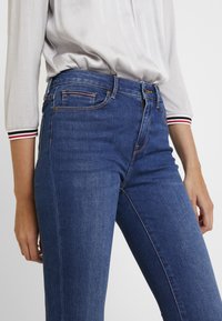 Blauwe denim jeans met een slim fit, een klassiek vijf-pocket ontwerp, subtiele vervaging en contrasterende stiksels, gecombineerd met een lichtgrijze top.