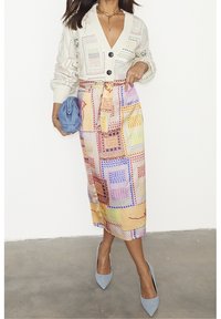 Cremfarbener gestrickter Cardigan mit großen Knöpfen, kombiniert mit einem bunt gemusterten Bleistiftrock und hellblauen High Heels.