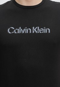 Μαύρο T-shirt με στρογγυλή λαιμόκοψη με το λογότυπο "Calvin Klein" σε λευκή και γκρι γραμματοσειρά, κεντραρισμένο στο στήθος.