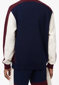 Sudadera azul marino con mangas en bloques de color granate y crema. Textura suave, puños acanalados y cuello redondo. Corte casual.