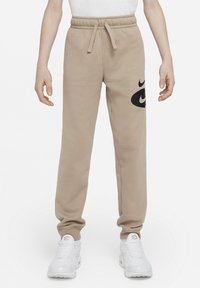 Béžové tepláky s elastickým pasem a stahovací šňůrkou, s černým logem Nike na levé nohavici. Vyrobené z měkké, texturované látky.