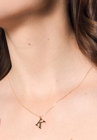 Złocony naszyjnik z zawieszką w kształcie litery "K", spoczywający na delikatnym łańcuszku, podkreślający finezyjne detale.