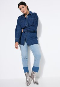 Camicia di jeans, blu scuro, abbottonata con maniche lunghe. Jeans azzurri con orlo blu scuro, abbinati a stivaletti metallici argento alla caviglia.
