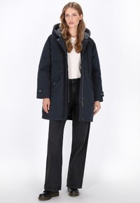 Marine parka jas met capuchon, twee zijzakken en ritssluiting. Gestructureerde stof en warme binnenvoering. Gecombineerd met zwarte flared jeans.