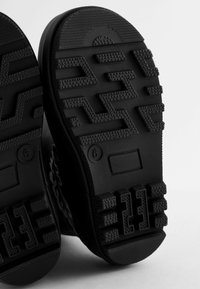 Semelles de bottes en caoutchouc noir avec un motif de bande de roulement texturé, présente des accents ridés et des détails circulaires pour l'adhérence et la stabilité. Taille indiquée comme 6.