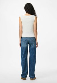 Top a spalline bianco a coste abbinato a un paio di jeans denim blu larghi. I jeans presentano un design classico a cinque tasche e una vestibilità comoda.