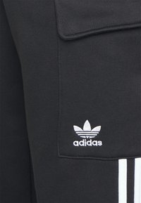 Svarta sweatpants i bomullsmix, med en framficka, vitt adidas-logotyp och tre vita ränder längs sidorna.