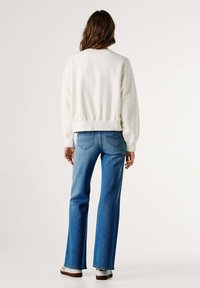 Sudadera blanca de algodón con dobladillo acanalado, combinada con vaqueros azules acampanados que presentan un diseño clásico de cinco bolsillos y detalles sutiles de costura.