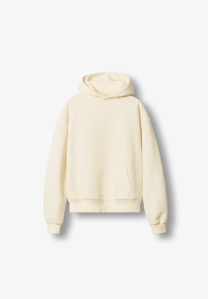 Kreminės spalvos kapučino striukė, pagaminta iš minkštos medžiagos, turi didelę priekinę kišenę, ilgas rankoves ir reguliuojamą raištelį kapuche.