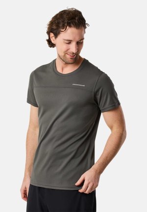 Mand iført mørkegrå atletisk kortærmet skjorte med "Swedemount" logo, kigger ned og smiler mod en hvid baggrund.