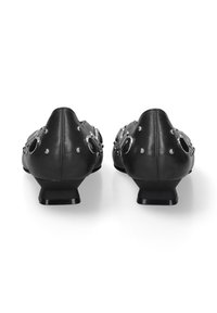 Zwarte leren schoenen met een lage hak, voorzien van cirkelvormige metalen accenten en studs op de bovenkant, die een unieke geometrische vorm benadrukken.
