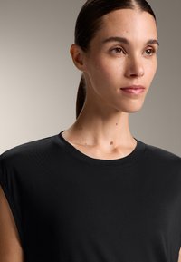 Top senza maniche nero con scollo rotondo, realizzato in un tessuto liscio e a costine. Presenta linee pulite e una silhouette aderente.