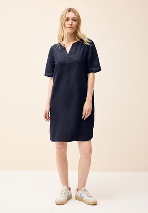 Marinblå linnekjol med V-hals och korta ärmar, kompletterad med off-white sneakers med blå accenter och en strukturerad sula.