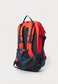 Mochila en rojo y marino con correas ajustables, respaldo acolchado, bolsillos con cremallera y almacenamiento lateral. Fabricada con un tejido duradero y con una forma estructurada.