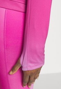 Top a manica lunga aderente in tessuto rosa sfumato, con cuciture eleganti e polsini con foro per il pollice per una maggiore comodità e mobilità.