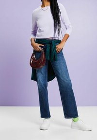 Světle fialový svetr s dlouhým rukávem, modrozelená košile zavázaná v pase, modré džíny s rovnými nohavicemi, bílé tenisky a vínová kabelka.