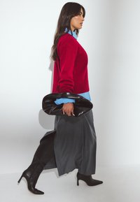 Raudona megzta palaidinė, šviesiai mėlynas marškinėlių apykaklė, pilka midi sijonas, juodi smailiakakliai auliniai batai ir juoda rankinė, demonstruojanti modernią siluetą.