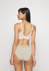Light pink bralette with adjustable straps and a low back design, paired with high-waisted beige panties featuring a lace trim.