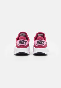 Nike sneakers i pink og rød med hvide såler, der har en polstret hæl, mesh-stof og fremtrædende sort branding på hæl-luppen.